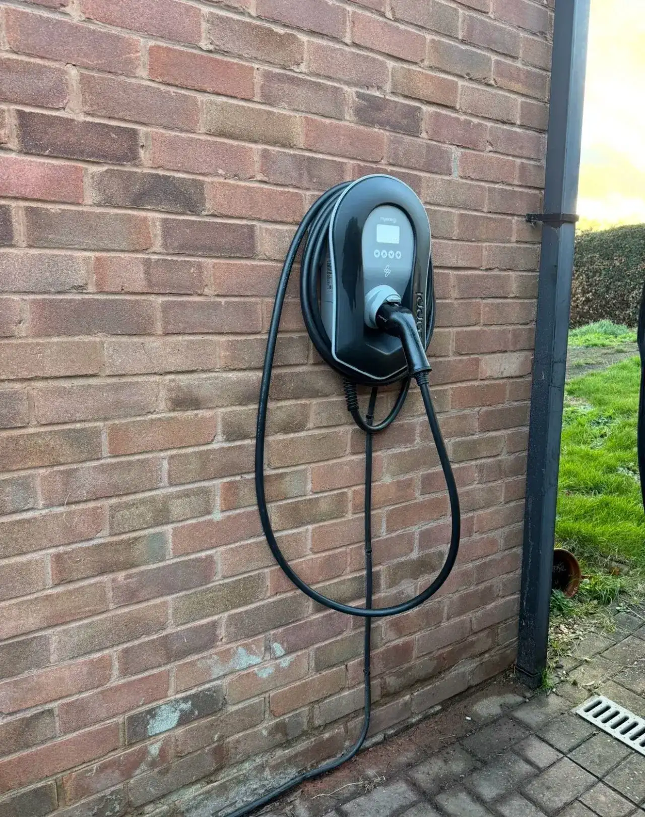 Black myenergi Zappi home EV charger neatly mounted on a residential brick wall with its cable stored in the integrated holster