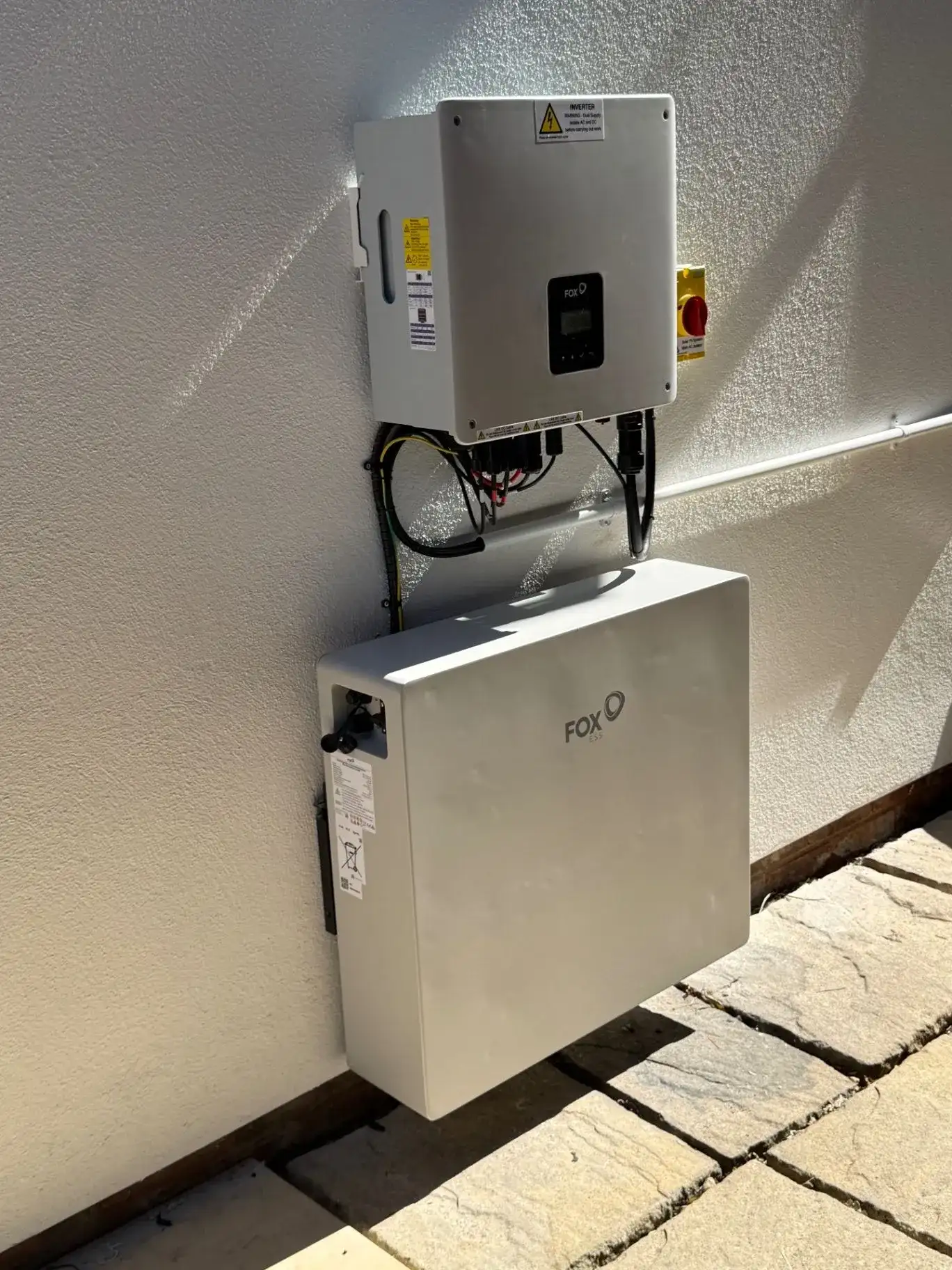 Fox ESS inverter above a white battery storage unit with visible cabling