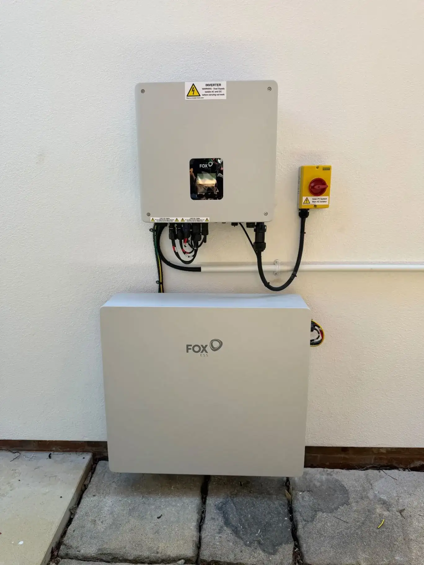 Wall-mounted inverter above a white battery storage unit beside a red isolator